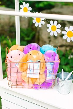 some stuffed animals are in a basket on a white table with flowers and daisies