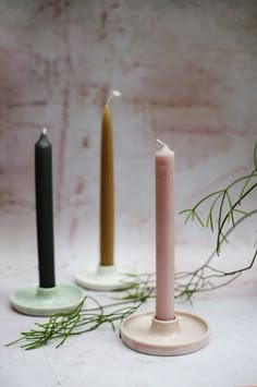 two candles are sitting next to each other on a white surface with greenery in the background