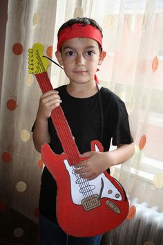 a young boy holding a red guitar shaped like a headband and wearing a bandana