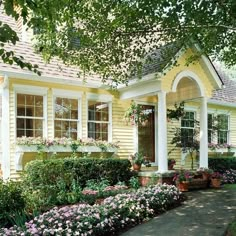 a yellow house with lots of flowers in the front yard