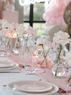 the table is set with pink and white flowers in glass vases, candles and plates