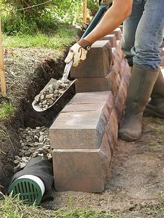 a woman is placing bricks into the ground to build a garden wall and planter