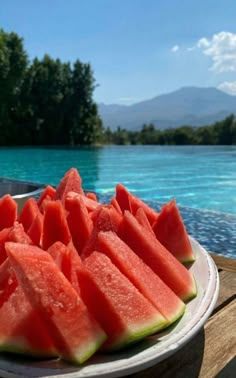 slices of watermelon sit on a plate next to a lake with trees in the background