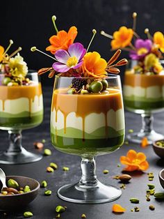 three desserts with flowers in them sitting on a black counter top, one is green and the other is orange