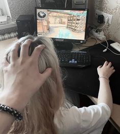 a woman sitting at a desk playing a video game on a computer monitor and keyboard