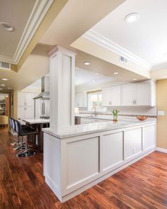 a large kitchen with an island in the middle and white cabinets on both sides, along with hardwood flooring