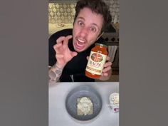 a man holding a bottle of hot sauce in front of a bowl with food on it