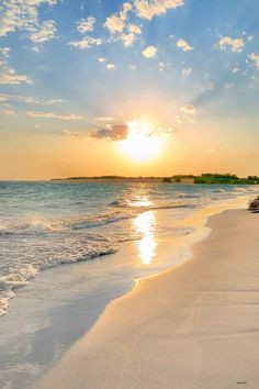 the sun is setting over the water at the beach with white sand and blue skies