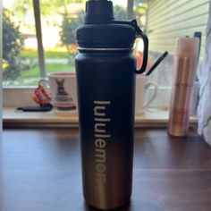 a black water bottle sitting on top of a wooden table in front of a window