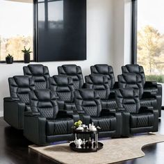 a row of black leather reclining chairs in front of a wall mounted screen and large windows