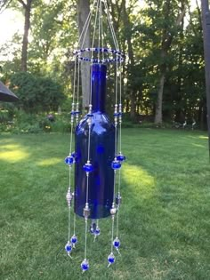 a blue vase with beads hanging from it's side in the grass near trees