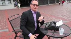 a man in a suit sitting at a table with a laptop computer on top of it