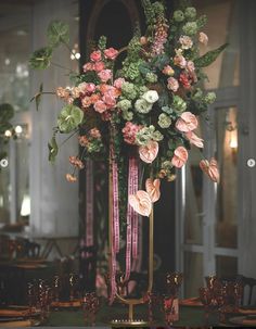 a tall vase filled with pink and green flowers on top of a table next to candles