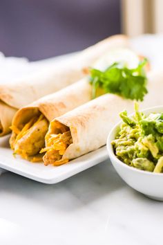 two burritos on a plate with guacamole and cilantro