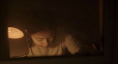 a woman looking at her cell phone in the dark with a lit candle behind her