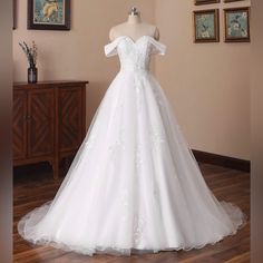 a white wedding dress on display in a room with wooden flooring and framed pictures