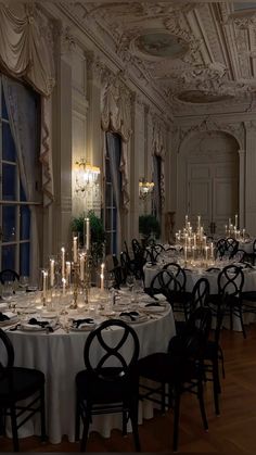 a dining room filled with lots of tables covered in white tablecloths and centerpieces