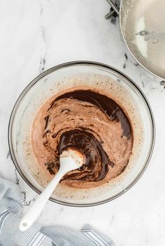 a mixing bowl filled with chocolate frosting next to two silver pans on a marble counter