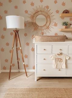 a baby's room with floral wallpaper and wooden flooring, a white dresser topped with a t - shirt