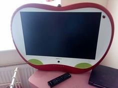 an apple shaped computer monitor sitting on top of a pink table next to a laptop