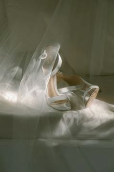 a pair of white high heel shoes sitting on top of a bed covered in plastic