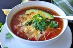 a white bowl filled with soup and topped with avocado, cheese and cilantro