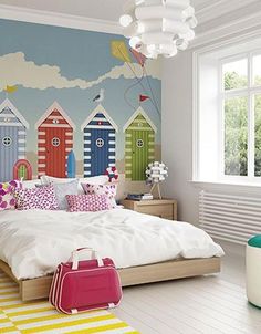 a bedroom decorated with colorful beach huts painted on the walls and floor, along with a pink suitcase