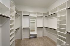 an empty walk in closet with white shelving and shelves on the wall, along with carpeted flooring