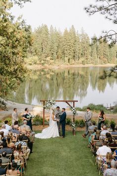 a couple getting married in front of a lake and surrounded by people sitting at chairs