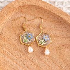 a pair of earrings with flowers and pearls hanging from them on top of a wooden surface