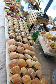 many different types of sandwiches are lined up on a long table with other food items in the background