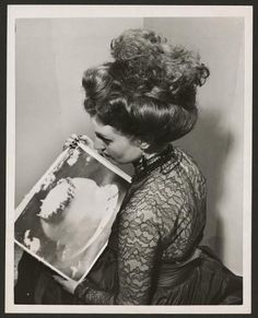 an old black and white photo of a woman holding a book with her face close to the camera