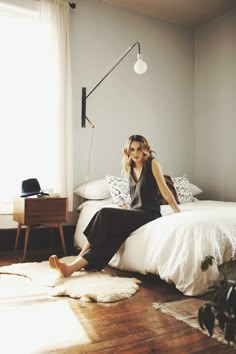 a woman sitting on top of a bed next to a lamp and a window in a room