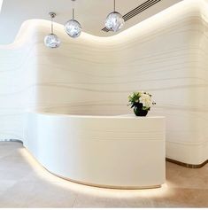 a white curved reception counter with flowers in a vase on the top and lights hanging from the ceiling