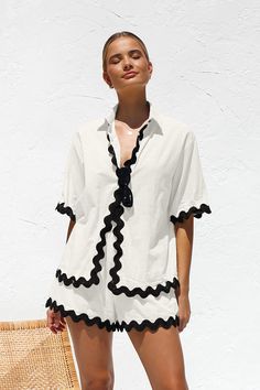 a woman standing in front of a white wall wearing a black and white shirt dress