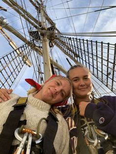 two girls standing next to each other in front of a tall ship with sails and ropes