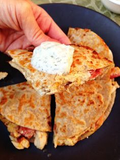 a hand holding a piece of quesadilla on top of a black plate