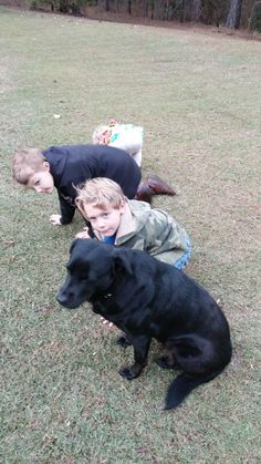 two boys and a black dog laying in the grass