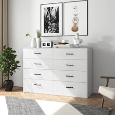 a white dresser with two pictures on the wall and a potted plant next to it