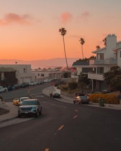 cars are parked on the street in front of houses and palm trees as the sun sets