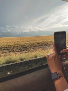 a person is taking a photo on their cell phone while riding in a vehicle with mountains in the background