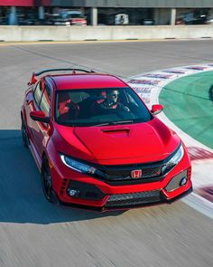 a red honda civic type car driving on a race track with people in the driver's seat