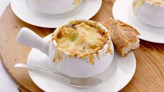 three white dishes filled with food sitting on top of a wooden tray next to bread