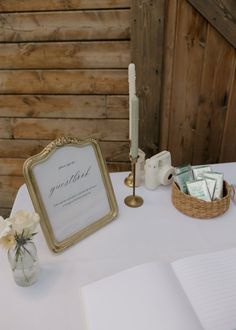 a white table with a gold framed sign and flowers on it, next to an open book