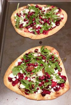 two pizzas with spinach, cheese and cranberry sauce on baking sheet