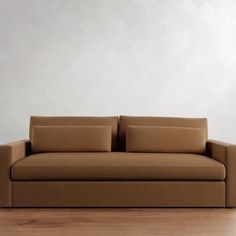 a brown couch sitting on top of a wooden floor next to a white wall in an empty room