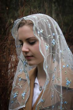 a woman wearing a veil with blue flowers on it and a brown jacket over her shoulders