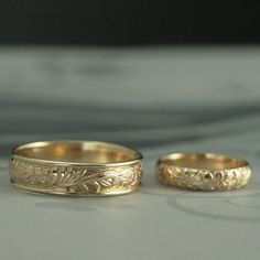 two gold wedding rings sitting on top of a white table next to each other,