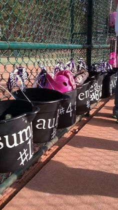 several buckets with helmets are lined up on the side of a tennis court fence