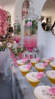 a table topped with lots of glasses filled with pink liquid and lemons next to a pitcher